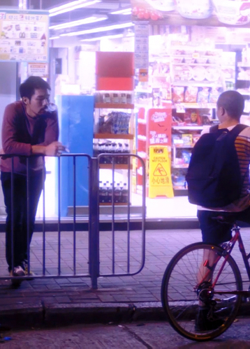 Filmstill aus I miss you when I see you, ein Mann sieht einem anderen mit Fahrrad auf der nächtlichen Straße an